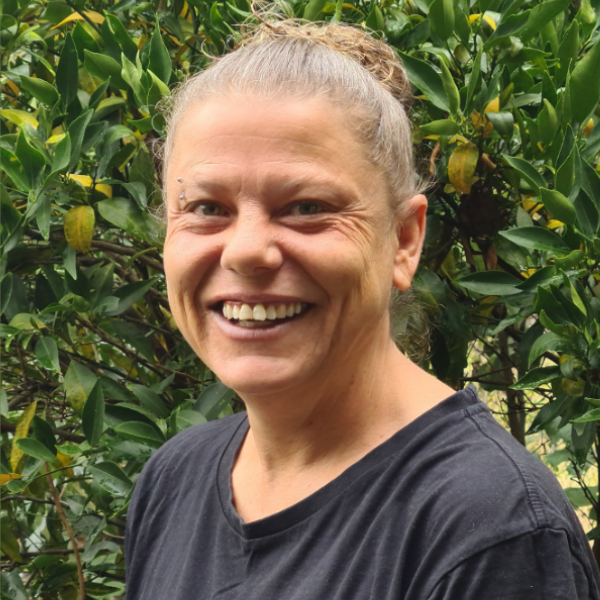 Headshot of woman. Green leafy tree behind her.