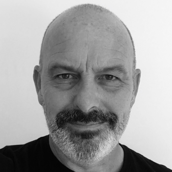 Headshot of author Andrew Daddo with short, salt-and-pepper hair and a warm smile. He is wearing a dark navy blue t-shirt and is positioned against a clean white background.